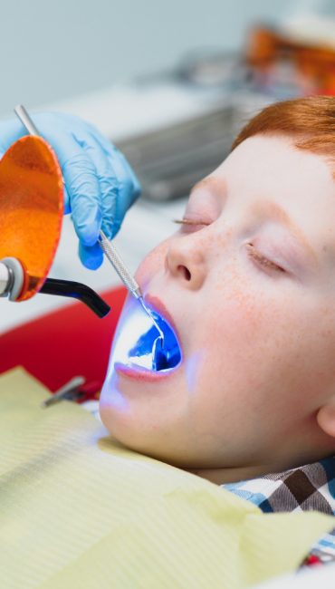 dentista-usando-mascara-dentista-infantil-ruivo-usando-mascara-examinando-menino-bonito